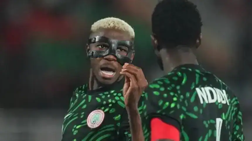 Des joueurs nigérians en maillot vert à motifs traditionnels, dont un portant un masque de protection, engagés dans une conversation animée pendant un match.