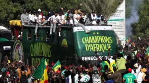 Célébrations au Sénégal où les supporters se rassemblent autour d'un bus arborant l'inscription "Champions d'Afrique", illustrant la fierté footballistique et l'unité nationale.