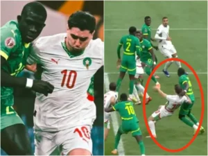 Un joueur marocain portant le numéro 10 est fauché par un défenseur sénégalais lors d'un match intense, illustrant l'esprit compétitif du football africain.