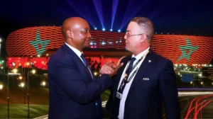 Two officials engage in conversation outside a brightly lit stadium featuring Moroccan colours, showcasing unity ahead of a major football event.