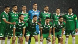 لاعبو نادي الرجاء البيضاوي يلتقطون صورة جماعية بقمصان خضراء، مع حارس مرمى أزرق، قبل مباراة مهمة، مما يظهر وحدة الفريق واستعداده.