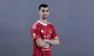 Un footballeur marocain pose dans un maillot rouge d'Al Ahly rehaussé de blanc, les bras croisés, sur fond gris.