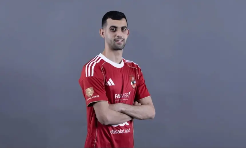 Un footballeur marocain pose dans un maillot rouge d'Al Ahly rehaussé de blanc, les bras croisés, sur fond gris.