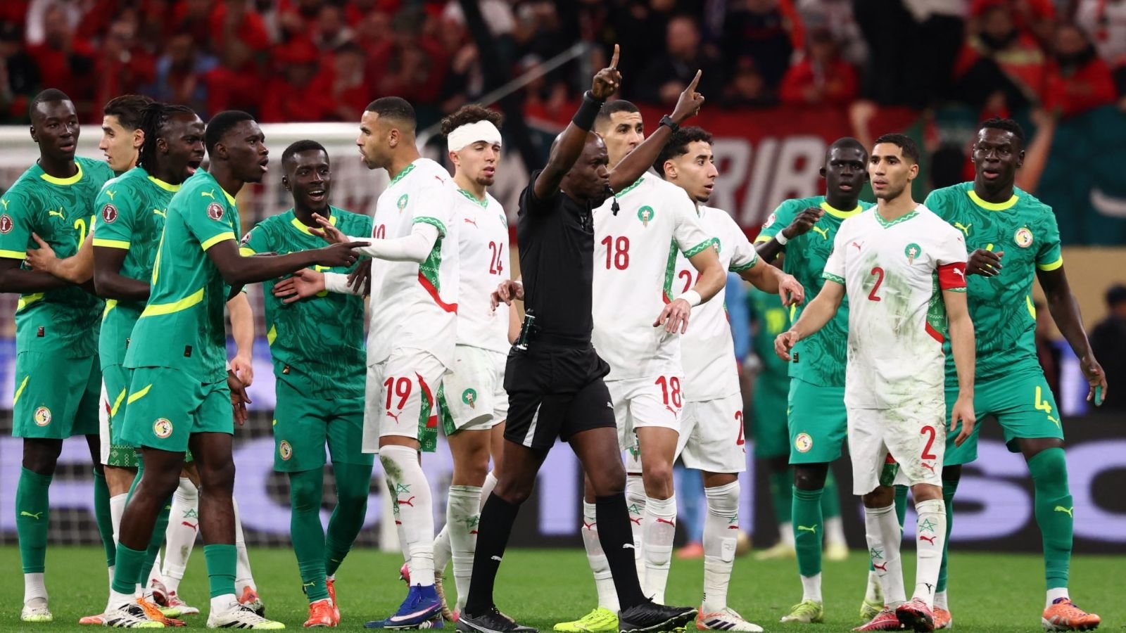Morocco and Senegal players clash during a tense moment in the match, while the referee intervenes amid a vibrant stadium atmosphere.