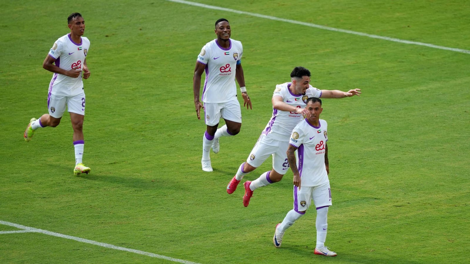 لاعبو الوداد يحتفلون بهدف في الملعب، مرتدين قمصان بيضاء مع لمسات أرجوانية، مما يظهر روح الفريق والإثارة خلال المباراة.