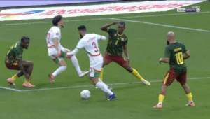 Abde dribble past les défenseurs camerounais dans un match palpitant, montrant agilité et compétence dans un cadre de tournoi international vibrant.
