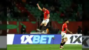 Les joueurs égyptiens célèbrent sur le terrain pendant un match, l'un d'eux bondissant de joie en portant un maillot rouge, illustrant l'esprit d'équipe.
