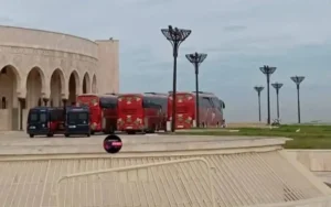 Red team buses parked outside a grand building in Casablanca, surrounded by decorative streetlights and open grass areas.