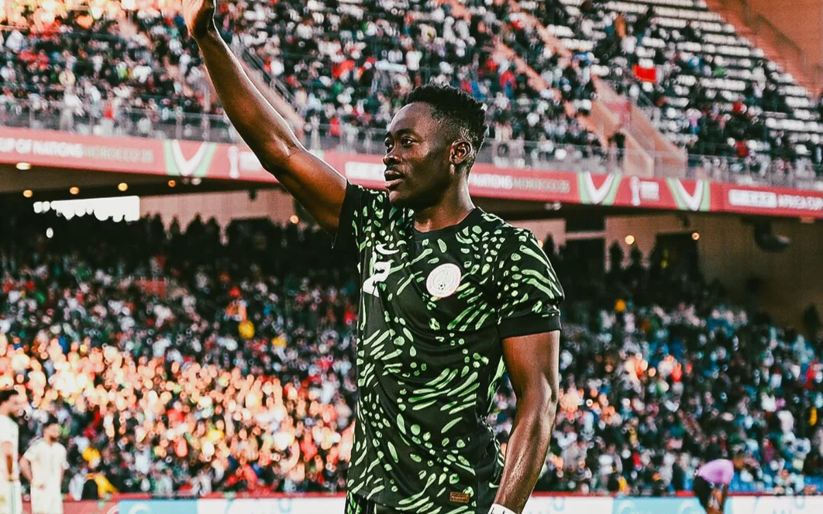 Un joueur nigérian fait un geste vers la foule dans un kit vert vif, sur fond de fans en train d'applaudir pendant la Coupe d'Afrique des Nations.