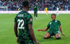 Les joueurs nigérians célèbrent un moment crucial lors de la demi-finale de la Coupe d'Afrique, portant des maillots verts distinctifs avec une foule animée en arrière-plan.