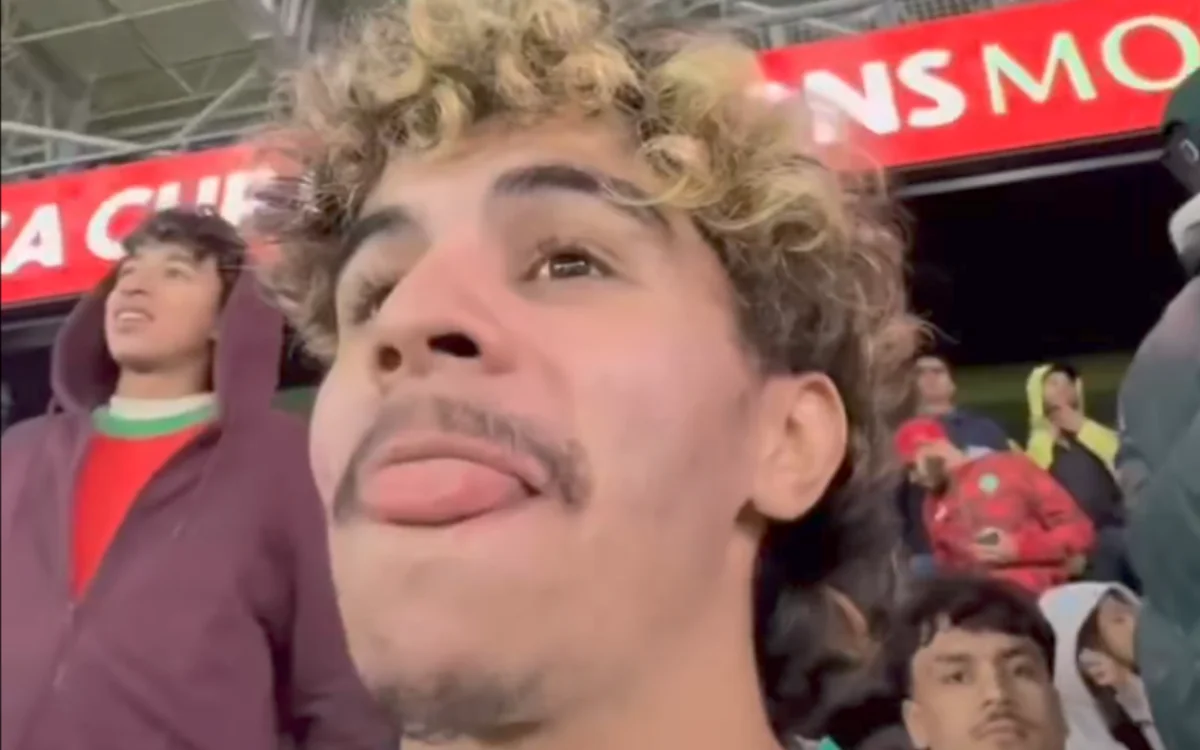 Moroccan football fans express excitement in the stadium, with one supporter showing a playful gesture and curly hair, amidst a vibrant crowd.