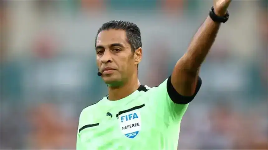 FIFA referee in bright green kit signals during a match, displaying authority and focus, with a blurred stadium background.