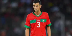 Un joueur marocain portant un maillot rouge avec des accents verts et le numéro 3, concentré sur le terrain pendant un match.