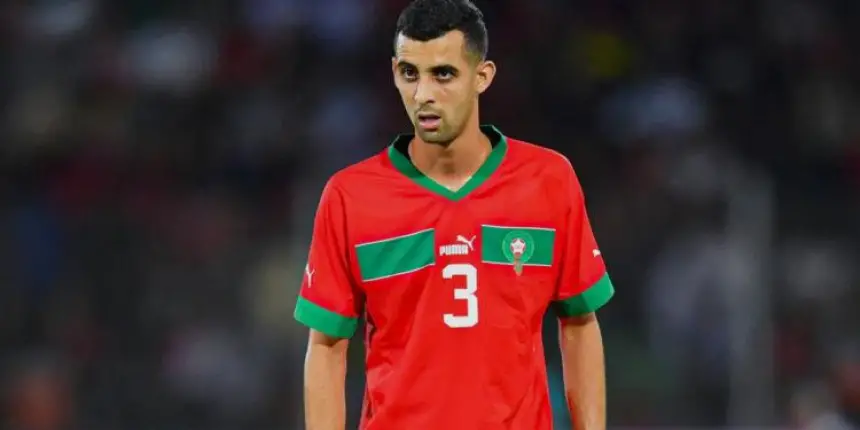 Un joueur marocain portant un maillot rouge avec des accents verts et le numéro 3, concentré sur le terrain pendant un match.