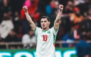 Brahim Diaz celebrates with raised fists, wearing the Moroccan national team jersey featuring the number 10, amidst a vibrant stadium backdrop.