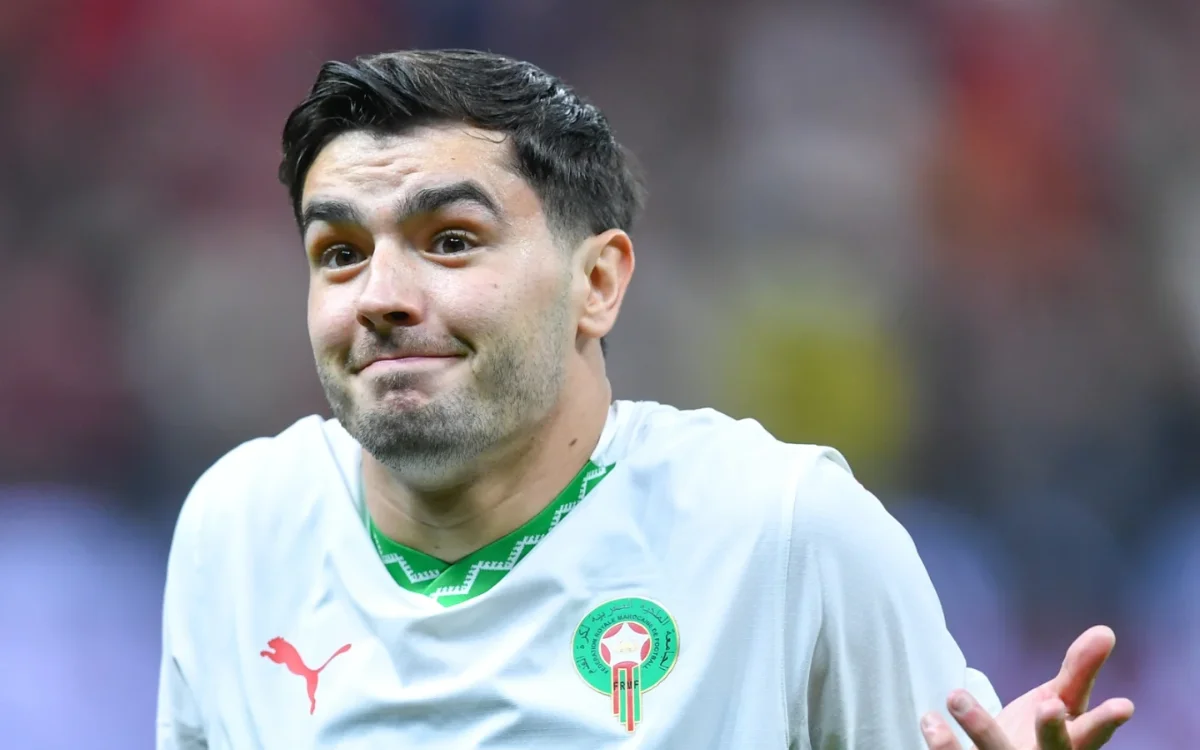 Brahim Diaz portant un maillot de l'équipe nationale marocaine blanc avec une expression perplexe pendant un match, montrant l'emblème de l'équipe.