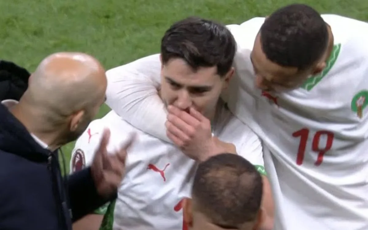 Brahim Diaz, visibly emotional, is comforted by Moroccan teammates and coach after a match, wearing the team's white kit with red accents.