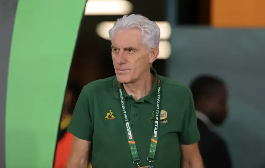 Coach in a green polo shirt with CAF lanyard, walking through a stadium, focused and determined ahead of a match.