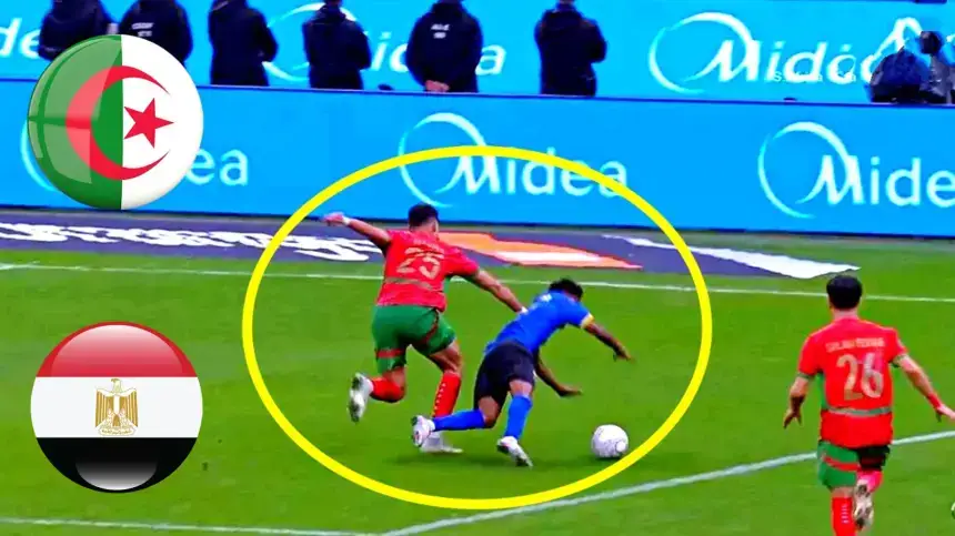 Un joueur portant un maillot vert et rouge tacle un adversaire en maillot bleu, avec les drapeaux de l’Algérie et de l’Égypte dans les coins, dans une scène de match.