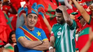 Des supporters marocains agitent des drapeaux en arrière-plan tandis qu'un joueur algérien, Riyad Mahrez, exprime sa déception, alors qu'un supporter congolais célèbre.