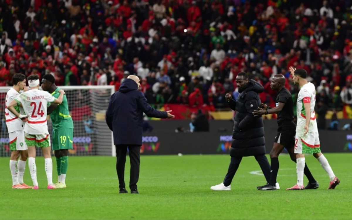 Moroccan and Senegalese players interact post-match, with a vibrant crowd in red visible. Tension amidst warm gestures highlights the rivalry.