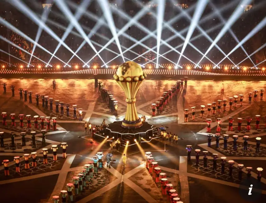 AFCON trophy surrounded by performers in vibrant costumes, illuminated by stage lights, creating a festive atmosphere for the tournament.