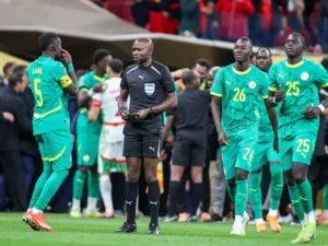 Les joueurs sénégalais en maillots verts se rassemblent autour d'un arbitre en noir, pendant un moment intense d'un match, illustrant la tension et la concentration.
