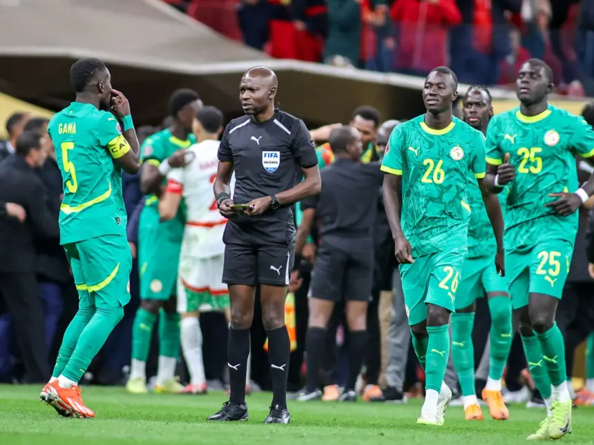 Les joueurs sénégalais en tenue verte, dont Gana, s'entretiennent avec l'arbitre vêtu de noir lors d'un moment tendu après un match.