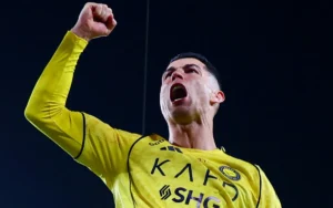 Cristiano Ronaldo celebrates triumphantly in a bright yellow Al Nassr kit, with a raised fist and an expression of joy.