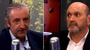 Two sports commentators engaged in a discussion, featuring one with grey hair in a navy suit and the other with a bald head and beard in a black suit, both in a studio setting.