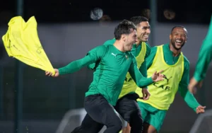 Moroccan players in green training kits laugh and celebrate, waving yellow training bibs during a lively training session ahead of the Africa Cup.