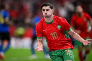 Moroccan forward celebrating in a vibrant red and green kit, displaying the number 10, during a match with fans in the background.