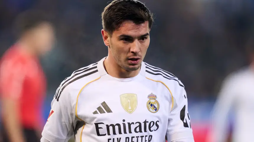 Real Madrid midfielder wearing the team's white kit, featuring the club logo, looking focused during a match with blurred players in the background.