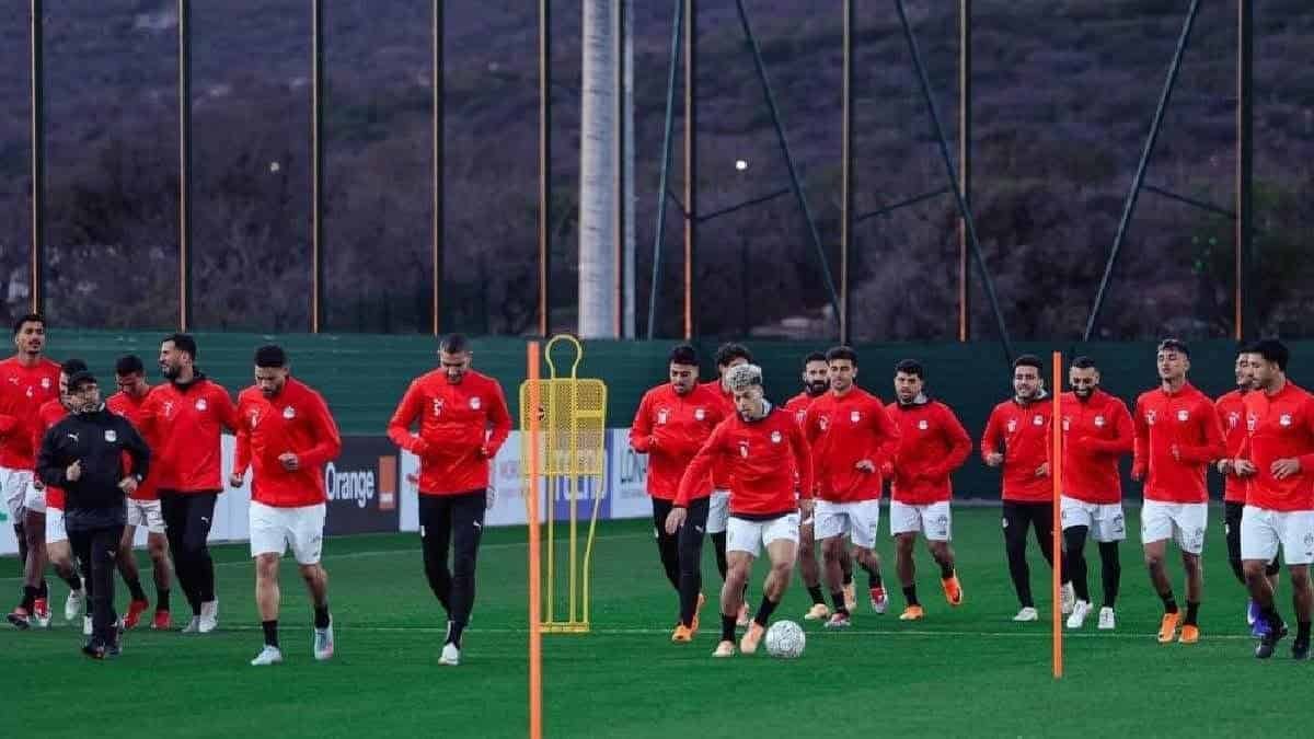 Egyptian national football team training, players in red kits practicing on a green pitch, focused on drills ahead of a competition.