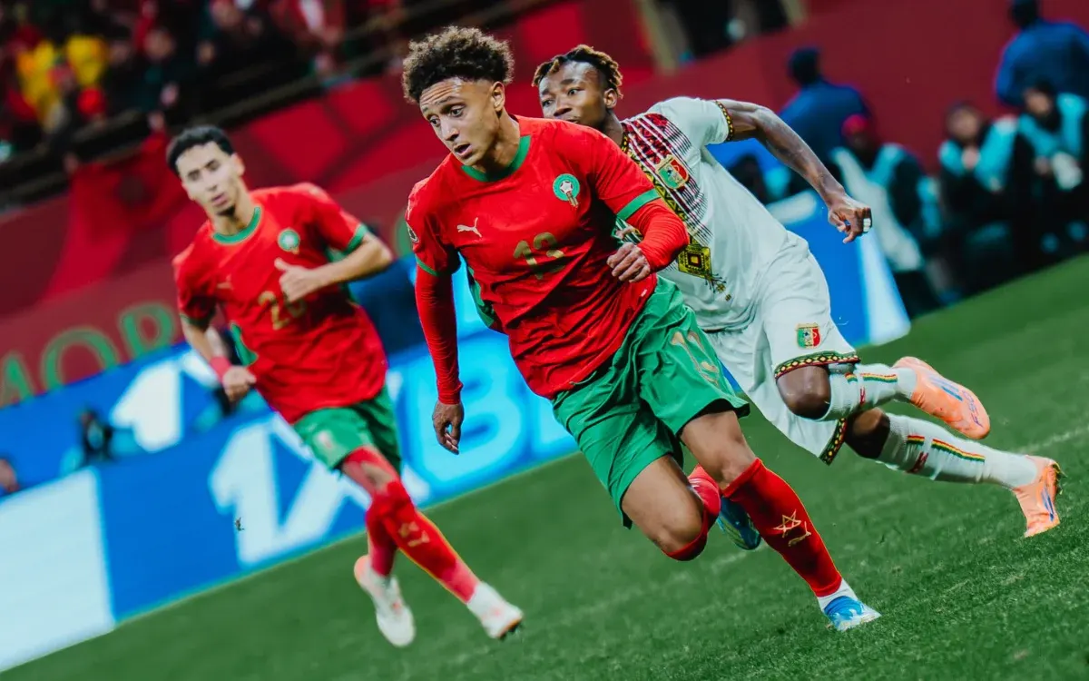 Eliesse Ben Seghir in a red Morocco kit sprints past a defender during an intense match against Mali, showcasing lively action on the pitch.