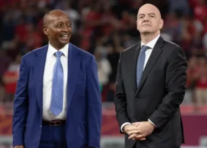 CAF-voorzitter Patrice Motsepe glimlacht naast FIFA-voorzitter Gianni Infantino tijdens een groot voetbalevenement, wat leiderschap in de sport toont.