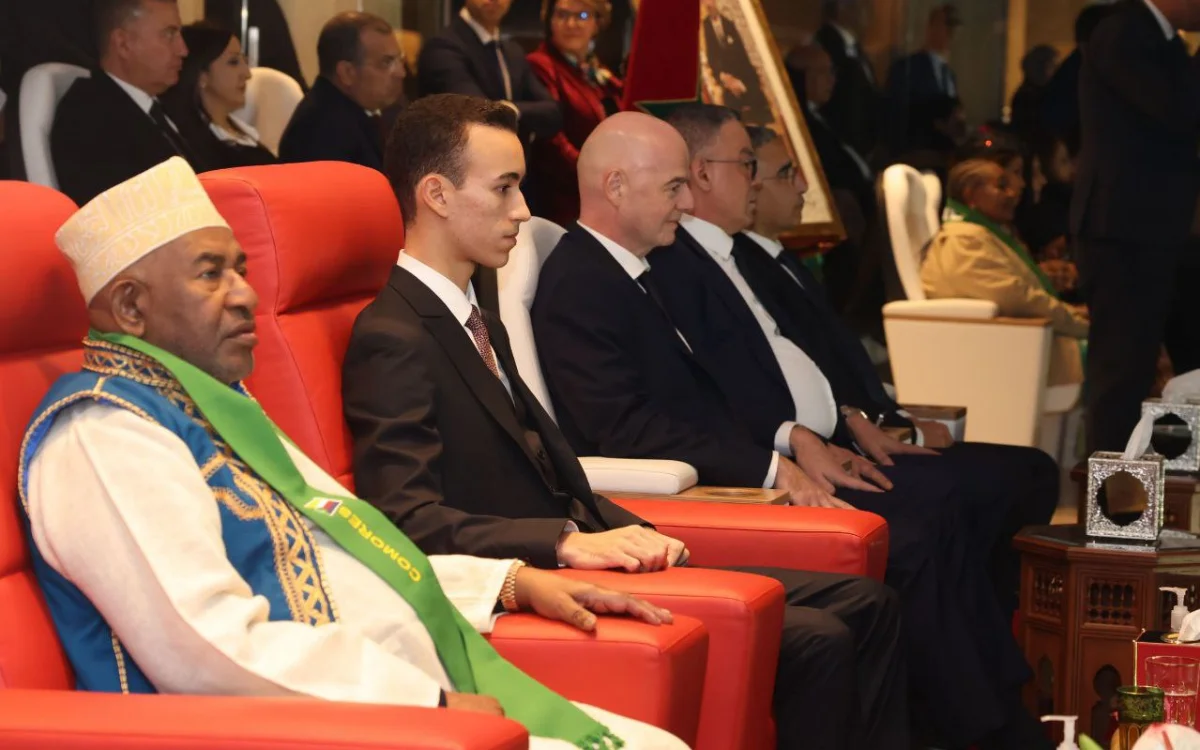 Gianni Infantino sits among dignitaries in red chairs at an event, showcasing a mix of formal attire and traditional garments.