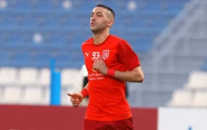 Hakim Ziyech, vêtu d'un maillot rouge arborant le numéro 93, trottine sur le terrain, prêt à entrer en action dans un stade aux sièges bleus.