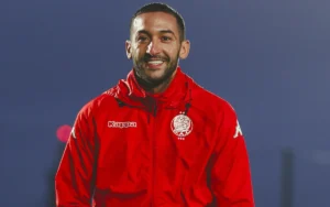 Hakim Ziyech smiles in a red Wydad Casablanca jacket during training, showcasing his enthusiasm and team spirit.