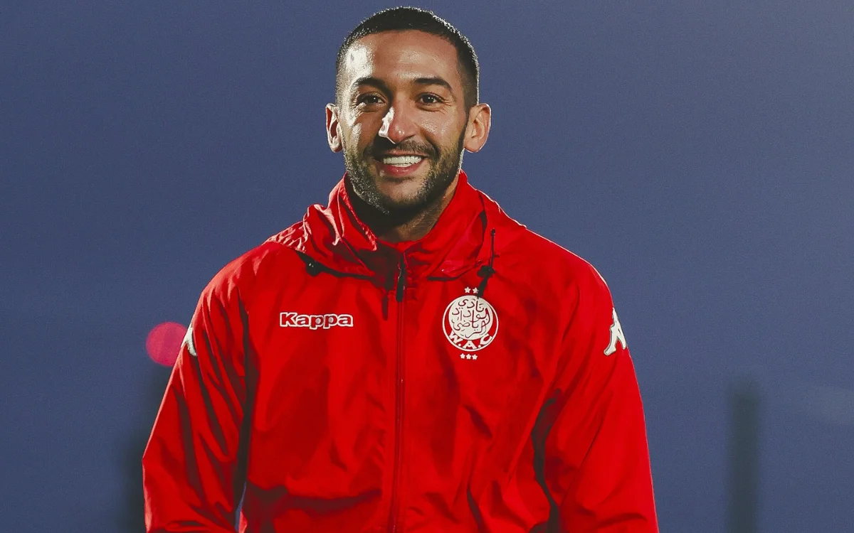 Hakim Ziyech smiles in a red Wydad Casablanca jacket during training, showcasing his enthusiasm and team spirit.