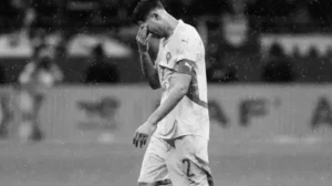 Achraf Hakimi, vêtu du maillot de l'équipe nationale marocaine, marche abattu, la main sur le front, sous la pluie qui l'entoure.