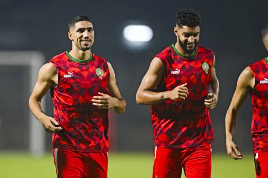 Achraf Hakimi en Selim Amallah tijdens de training, gekleed in het rood-groene Marokko-tenue, die een luchtig moment delen met teamgenoten.