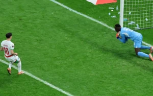 براهيم دياز، مرتديًا القميص رقم 10، يستعد لتسديد ركلة جزاء بنمط "بانينكا" بينما يراقبه حارس المرمى المنافس، في خلفية ملعب أخضر نابض بالحياة.