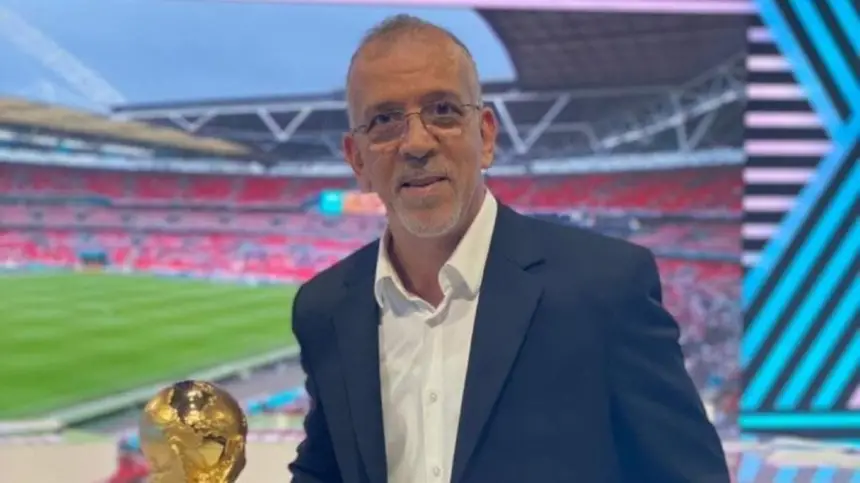 Une figure du football marocain tenant un trophée devant le stade de Wembley, portant un costume, avec des sièges de stade vibrants en arrière-plan.