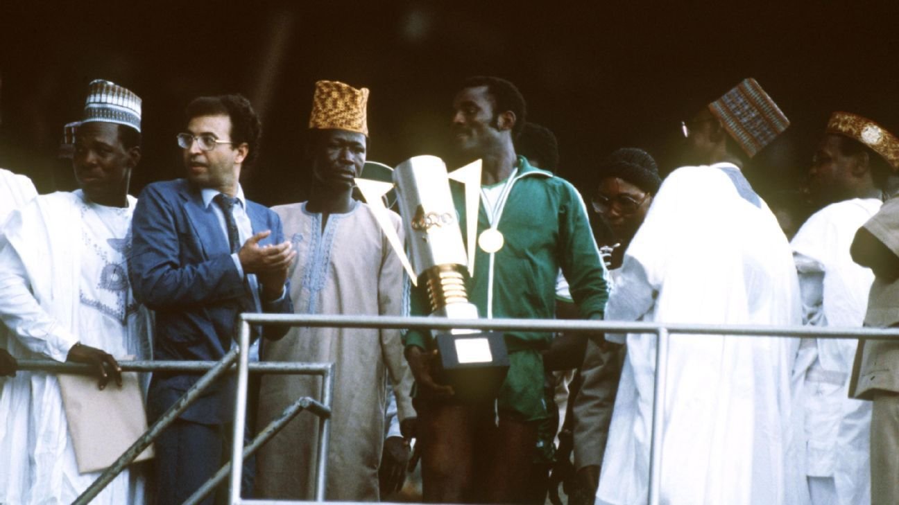 Un footballeur marocain brandit fièrement un trophée, entouré d'officiels et d'admirateurs, célébrant une victoire majeure lors d'un prestigieux événement.