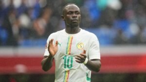Sadio Mané applaudit les fans, portant le maillot de l'équipe nationale du Sénégal en blanc avec des motifs colorés, lors d'un match sous la pluie.