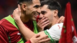Achraf Hakimi embraces Selim Amallah in celebration, both wearing their national team's colours, showcasing Moroccan camaraderie on the pitch.