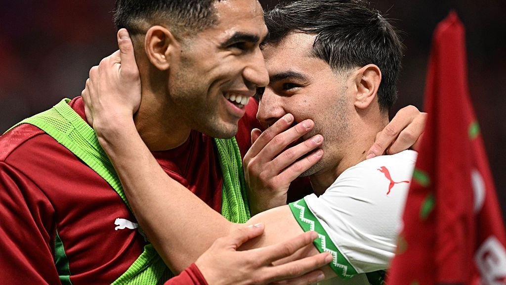 Achraf Hakimi embraces Selim Amallah in celebration, both wearing their national team's colours, showcasing Moroccan camaraderie on the pitch.