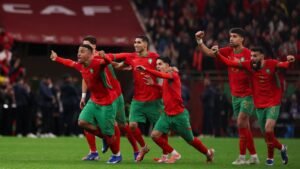 Moroccan players in red and green celebrate a goal, displaying joy and unity during a tense international match.