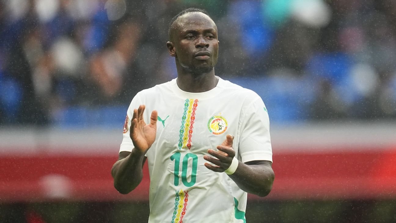 Sadio Mané applaudit les fans, portant le maillot de l'équipe nationale du Sénégal en blanc avec des motifs colorés, lors d'un match sous la pluie.